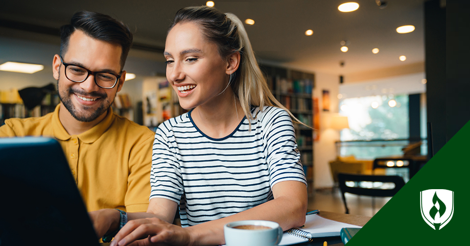 A female and male student talk while looking at a computer with a cup of coffee in the foreground