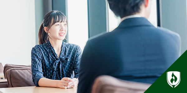 A woman in a dark blue polka dot shirt sits across from a male recruiter