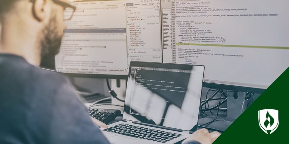 Programmer coding at desk with a laptop and two monitors