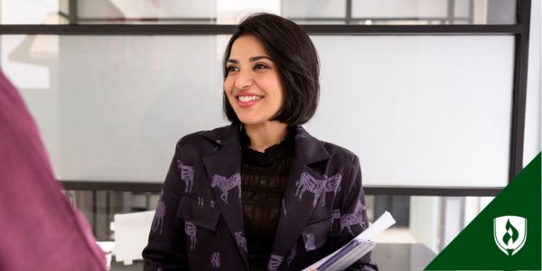 A financial analyst smiles at a colleague while holding a stack of documents