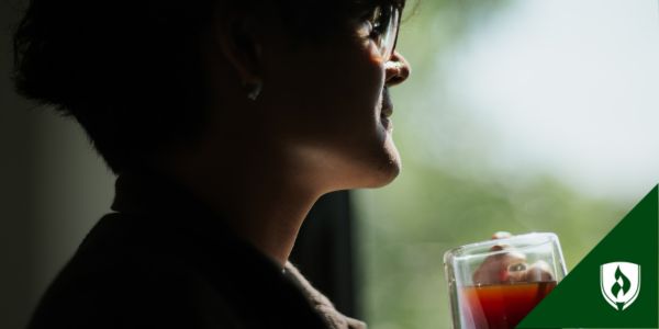 Someone stands at a window, silhouetted in shadow, drinking a cup of tea