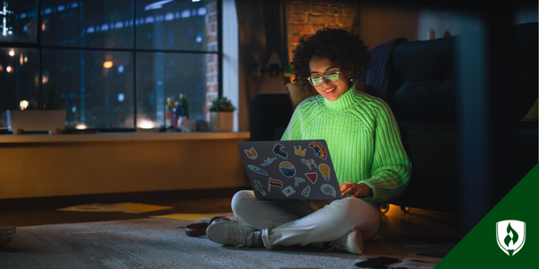 An online graphic design student sits on the floor, looking at her computer in a dark apartment