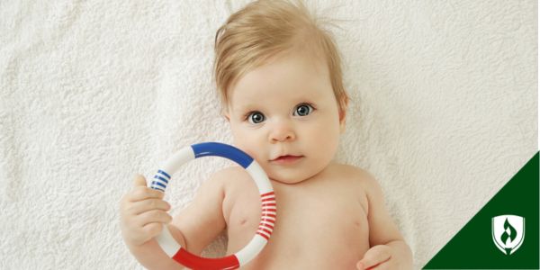 A sweet baby holds a toy ring on a white blanket