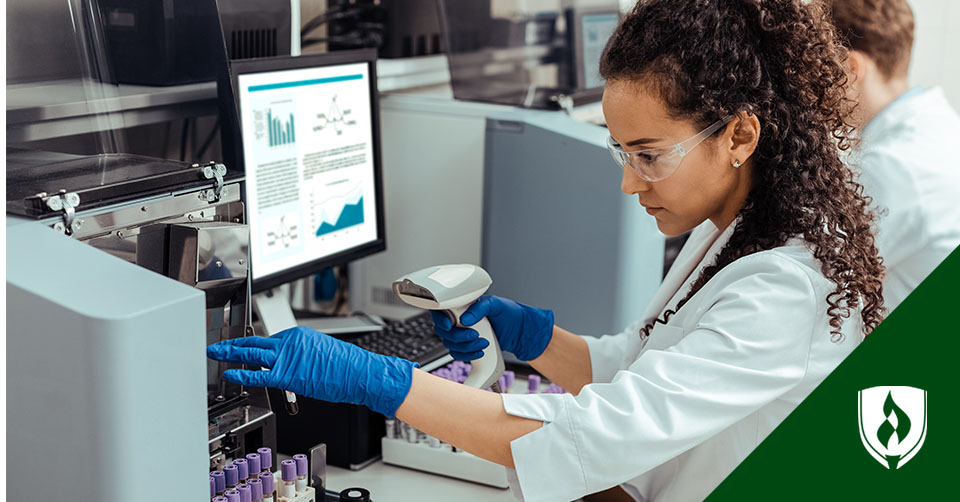 A woman with curly hair in a lab coat scans the code on a vial at her desk