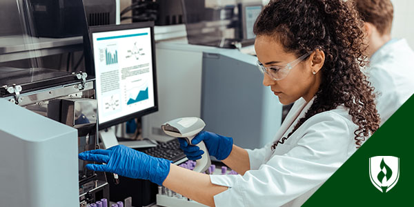 A woman with curly hair in a lab coat scans the code on a vial at her desk