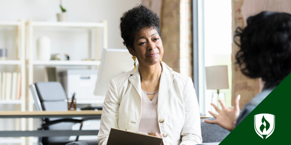 A black, female nurse practitioner in a white blazer listens to her patient