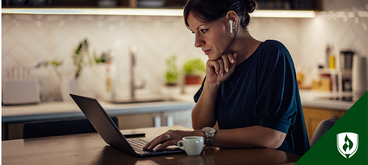 A Woman with ear pods works through an RN to BSN online course at her kitchen table at night