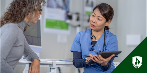 n Asian, female nurse in blue scrubs coaches a white, female patient