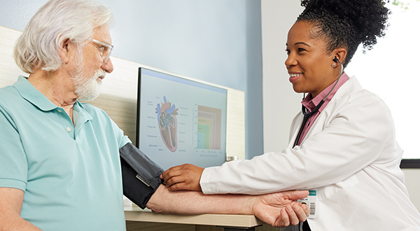 smiling female medical professional taking blood pressure on the arm of an elderly male patient